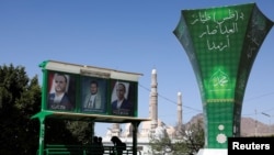 Sejumlah warga duduk di bawah poster yang menampilkan wajah dari pemimpin kubu Houthi di Sanaa, Yaman, pada 7 April 2022. (Foto: Reuters/Khaled Abdullah)