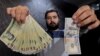 FILE - A money changer displays a U.S dollar, right, and the amount being given when converting it into Iranian rials at a currency exchange shop in Tehran's business district, Iran, Jan. 20, 2016. 