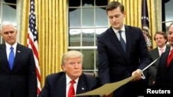 Le secrétaire du personnel de la Maison Blanche, Rob Porter, au centre, remet un document au président Donald Trump, à gauche, dans le bureau ovale de la Maison-Blanche, Washington, 20 janvier 2018.