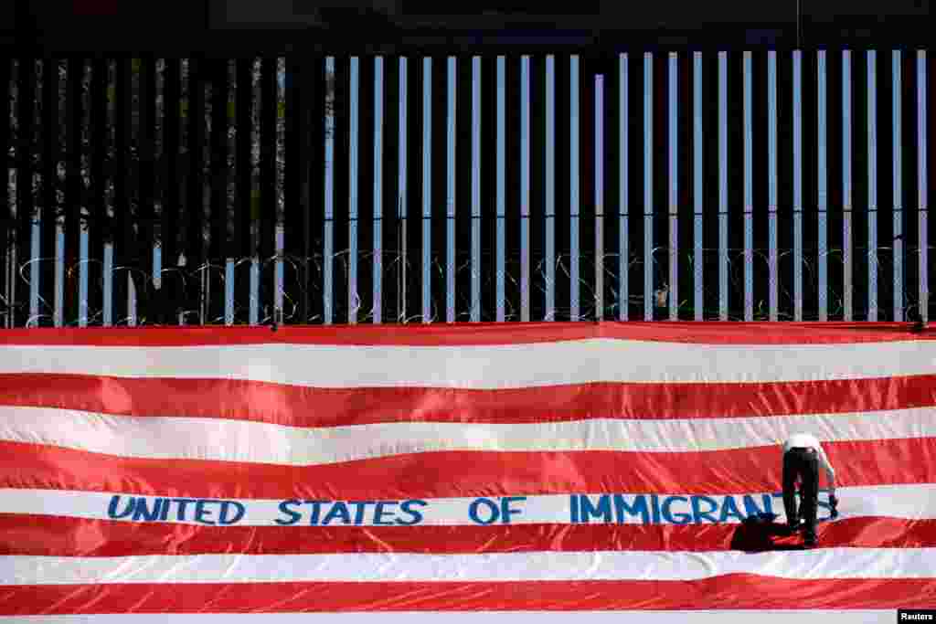 Roberto Marquez, known as Roberz, writes on a large U.S. flag as part of a protest called &#39;United States of Immigrants&#39; to demand respect for migrants, near a border wall in El Paso, Texas, as pictured from Ciudad Juarez, Mexico, June 6, 2019.
