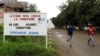 People jog past a sign, with a message by the M23 movement in their campaign against rampant corruption in the Democratic Republic of Congo, in an area under controlled of the Congolese Revolutionary Army (CRA) in Rutshuru town, November 3, 2012.