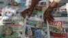 FILE - A newspaper vendor uses rocks to stop the day's front pages from blowing in the wind in Kano, northern Nigeria, Feb. 24, 2019.