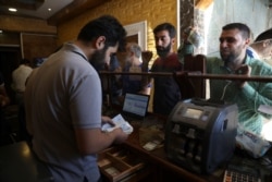 FILE - People exchange money in the city of Idlib, Syria, June 20, 2020. In the northwestern province of Idlib, the last remaining Syrian rebel stronghold, some people have started using the Turkish Lira instead of the Syrian pound.