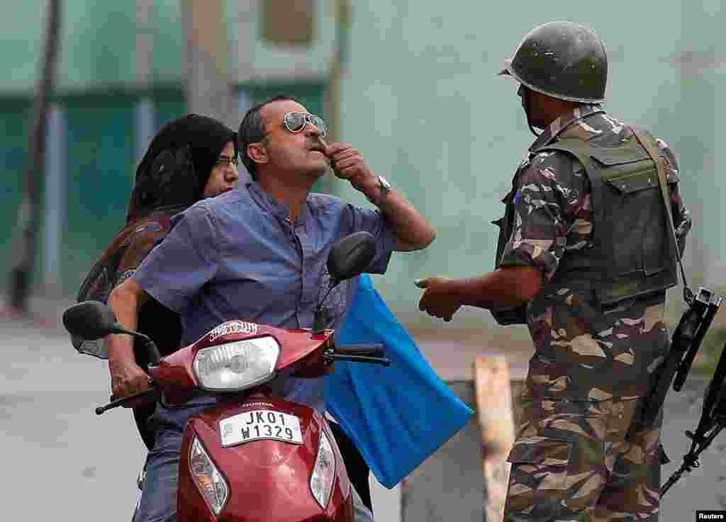 Seorang pria menunjukkan giginya yang sakit kepada polisi India saat ia minta izin pergi ke dokter gigi pada pemberlakuan jam malam di Srinagar, Kashmir-India.