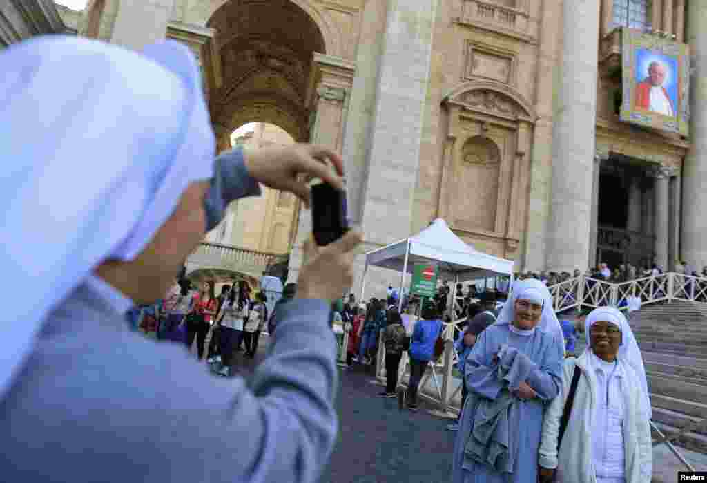 Dua biarawati berpose di depan tapestry yang&nbsp; menampilkan gambar Paus Yohanes Paulus II di St. Peter&#39;s Square di Vatikan. &nbsp;