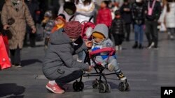 ​ແມ່​ຍິງ​ຄົນ​ນຶ່ງ​ເອົາ​ເຂົ້າ​ໜົມ​ໃຫ້​ລູກ​ກິນ​ຢູ່​ຖະ​ໜົນ​ຊັອບ​ປິ້ງ ຈ່​ຽນ​ເໝິນ, ນະ​ຄອນຫຼວງ ປັກ​ກິ່ງ, ຈີນ, 17 ມັງ​ກອນ 2023.(AP Photo/Andy Wong)