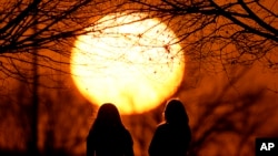 FILE - People watch the sunset at a park on an unseasonably warm day, Feb. 25, 2024, in Kansas City, Mo. (AP Photo/Charlie Riedel, File)