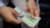 An Iranian man holds a stack of U.S. and Iranian bank notes. The Bonbast.com website, which tracks Iran’s unofficial exchange rates, showed the rial at a record low of 160,000 to the dollar on Sept. 24, 2018. (Photo Courtesy of Tasnim news agency)