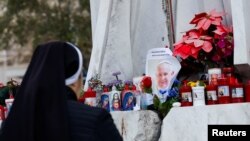 A nun prays as candles and flowers are placed at the base of the statue of the late Pope John Paul II outside the Gemelli Hospital where Pope Francis is admitted for treatment, in Rome, Italy, Feb. 23, 2025. 