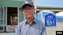  Kim Yoo-sung, 84, at the gate of his home that was severely damaged by the North Korean artillery attack. (Photo: VOA / Steve Herman) 