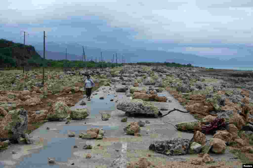 ស្រ្តី​ម្នាក់​ធ្វើ​ដំណើរ​នៅ​លើ​ផ្លូវ​ជាតិ​មួយ​គ្រប​ដណ្តប់​ដោយ​ដុំថ្ម​ បន្ទាប់​ពី​ការ​បោកបក់​នៃ​ព្យុះ​សង្ឃរា​ Matthew ទៅ​លើ​ខេត្ត​ Guantanamo នៅ​​​ប្រទេស​គុយបា។
