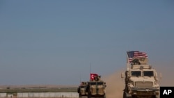FILE - Turkish and American forces conduct their first joint ground patrol in the so-called "safe zone" on the Syrian side of the border with Turkey, seen in the background, near Tal Abyad, Syria, Sept. 8, 2019.