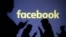 FILE - Silhouettes of mobile users are seen next to a screen projection of Facebook logo in this picture illustration taken March 28, 2018.