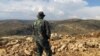 FILE - Hezbollah fighter looks toward Syria while standing in the fields of the Lebanese border village of Brital, Lebanon. 