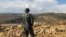 FILE - Hezbollah fighter looks toward Syria while standing in the fields of the Lebanese border village of Brital, Lebanon. 