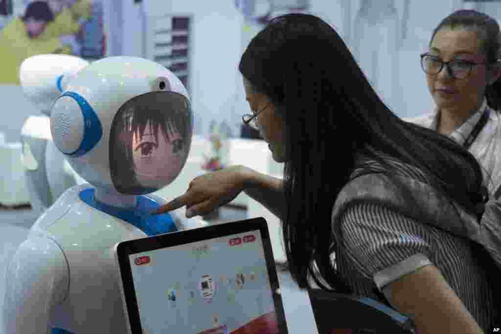 2018年6月15日在中国上海举行的2018亚洲消费电子展上，中国穿山甲机器人公司设计的机器人和参观者互动。中国大力研发机器人。