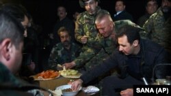 President Suriah Bashar al-Assad (kanan) berbagi makanan dengan tentara Suriah di garis terdepan, saat meninjau mereka di distrik Jobar, Damaskus, Suriah (31/12).