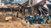 Emergency teams rest outside building with structural damage caused by heavy rains, July 9, 2018, in Hiroshima, Japan. 