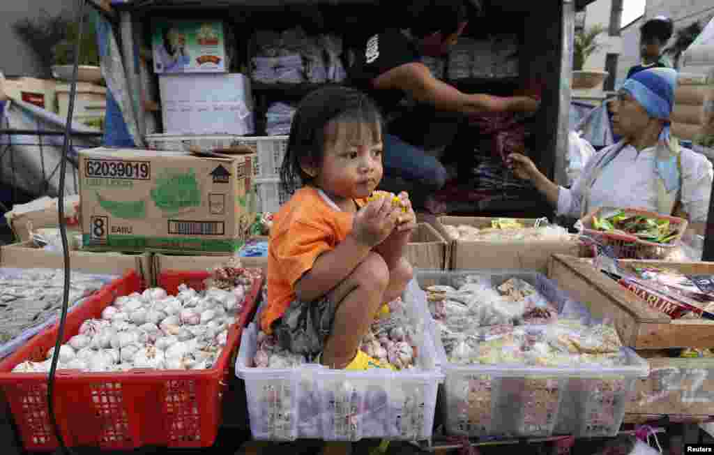 Seorang anak perempuan duduk di atas keranjang berisi bawang putih di sebuah pasar di Jakarta.