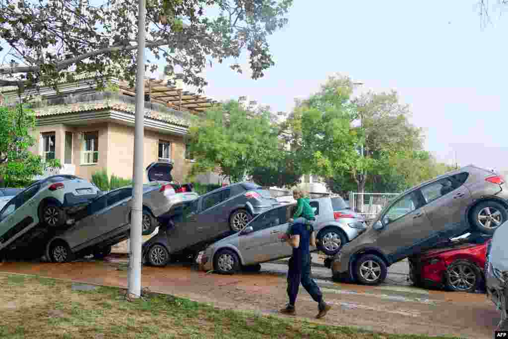 Residents walk past piled up cars following deadly floods in Valencia&#39;s De La Torre neighborhood, south of Valencia, eastern Spain. Floods triggered by torrential rains in Spain&#39;s eastern Valencia region have left at least 70 people dead.