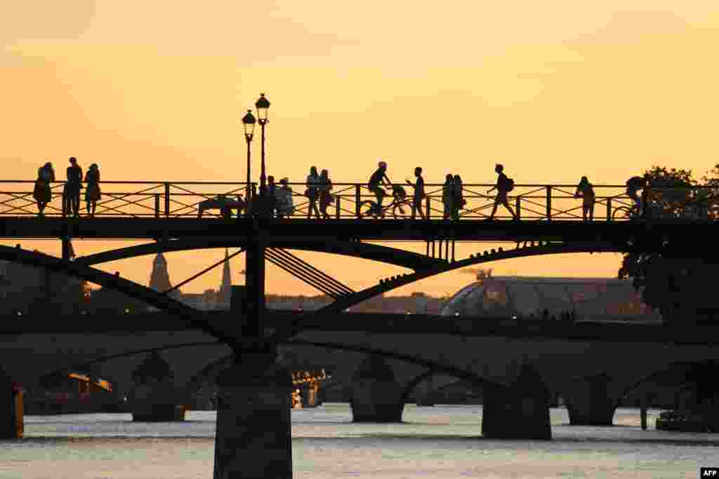 Para pejalan kaki dan pesepeda melintas di The Art Bridge yang melintang di atas Sungai Seine di Paris, Perancis saat matahari terbenam.