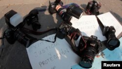 FILE - Journalists leave their cameras on posters demanding justice and protection during a protest against murder of Regina Martinez, journalist and correspondent for the Mexican magazine Proceso, in Puebla on April 29, 2012. 