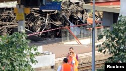 Para petugas tengah berdiri di dekat gerbong kereta yang longsor di stasiun kereta Bretigny-sur-Orge dekat Paris (13/7).