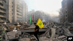 Foto ilustrasi yang menunjukkan seorang pria mengibarkan bendera Hizbullah di reruntuhan gedung apartemen di Lebanon pada 1 November 2024. (Foto: AFP/Hassan Ammar)