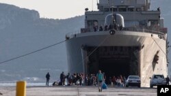 Migrants wait outside a military vessel after their disembarkation at the port of Elefsina, near Athens, on Saturday, Nov. 2, 2019.