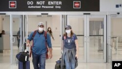 Mike Rustici, left, and Linda Scruggs exit customs after arriving on a flight from Lima, Peru, March 21, 2020, at Miami International Airport in Miami.