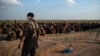 FILE - In this Feb. 22, 2019 file photo, U.S.-backed Syrian Democratic Forces (SDF) fighters stand guard next to men waiting to be screened after being evacuated out of the last territory held by Islamic State group militants, near Baghouz, eastern…