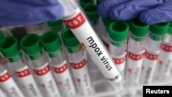 ພາ​ບນີ້​ສະ​ແດງ​ໃຫ້​ເຫັນ​ຫຼອດ​ທົດ​ລອງ​ກັບ​ປ້າຍ​ທີ່​ສະ​ແດງ​ໃຫ້​ເຫັນ​ການກວດ​ໂຣກ​ໝາກ​ສຸກ​ລີງ ຫຼື Mpox ເປັນ​ຜົນ​ບວກ.