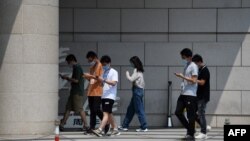 北京一群青年边走路边看手机。（2020年7月6日）