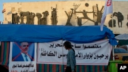 An anti-government protester walks by a defaced picture of Prime Minister-designate Adnan al-Zurfi in Tahrir Square, Baghdad, Iraq, March 19, 2020.