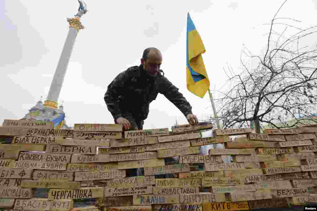 Seorang pria menumpuk batangan kayu bertuliskan nama-nama kota dan pemukiman Ukraina yang merupakan kampung halaman para demonstran, selama protes di Lapangan Kemerdekaan di Kiev, 16 Desember 2013.
