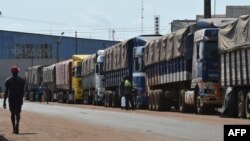 Des piétons passent devant des camions chargés de café pour l'exportation au port d'Abidjan, le 8 mars 2018