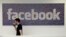 FILE - A Facebook employee walks past a sign at Facebook headquarters in Menlo Park, California. Britain's information commissioner tells BBC on Tuesday she is also investigating Facebook and has asked the company not to pursue its own audit of Cambridge Analytica's data use. She says Facebook has agreed.
