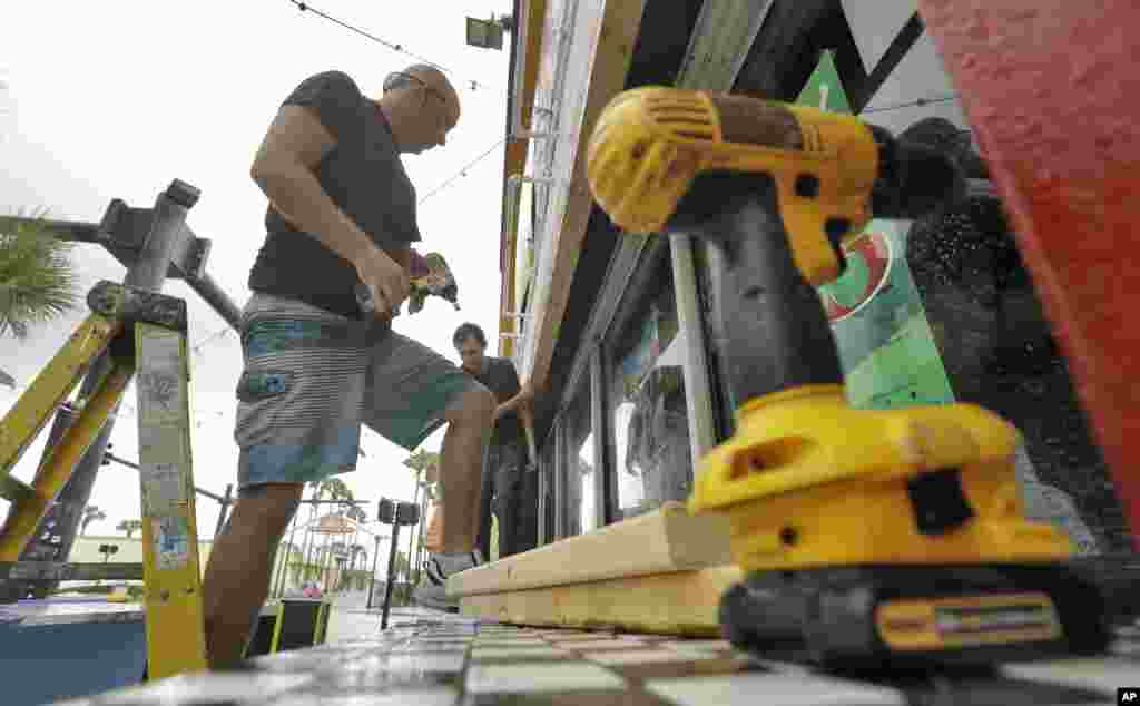 បុរស​ពីរ​នាក់​ដាក់​ផ្ទាំង​ឈើ​បិទ​រង្គសាល​មួយ​នៅ​លើ​តាម​បណ្តោយ​ឆ្នេរ Daytona រដ្ឋ Florida។ រង្គសាល​នេះ​គ្រោង​នឹង​បើក​ទទួល​អតិថិជន​អំឡុងពេល​ព្យុះ​សង្ឃរា Matthew។&nbsp;