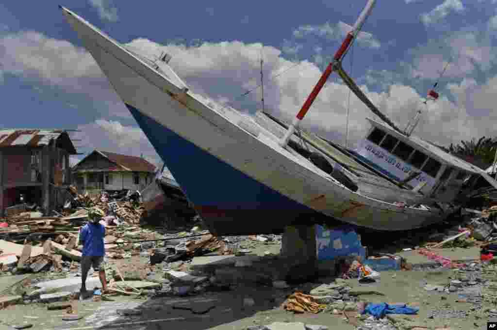 A man walks past a boat swept ashore by a tsunami in Wani village on the outskirt of Palu, Central Sulawesi, Indonesia.