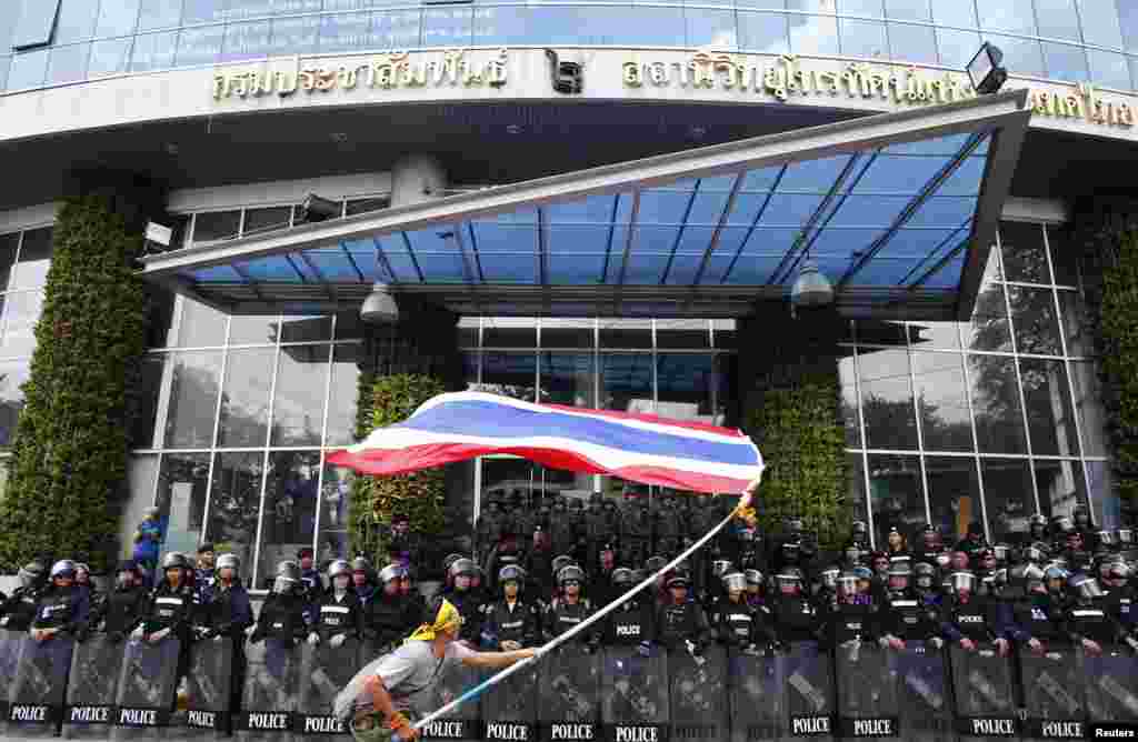 Para demonstran anti-pemerintah melambai-lambaikan bendera nasional di depan polisi anti-huru-hara dan tentara yang menjaga pintu masuk stasiun televisi National Broadcast Services of Thailand (NBT) di Bangkok (9/5). (Reuters/Athit Perawongmetha)