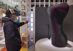 A robotic art installation called "Do Nothing with Al" mimics a person's slow movements. Here, the robot is following this man's hand. (Deborah Block/VOA)