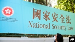 资料照：一名妇女走过香港街头宣传港版国安法的广告牌。（2020年6月30日）