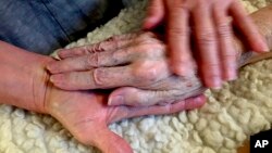 In this 2016 photo provided by Thomas Marrinson, Allison Beach holds the hand of her ailing mother Kathryne Beach inside her home in Hinesburg, Vt. Allison Beach and her husband struggled to figure out how to get help for her mother.