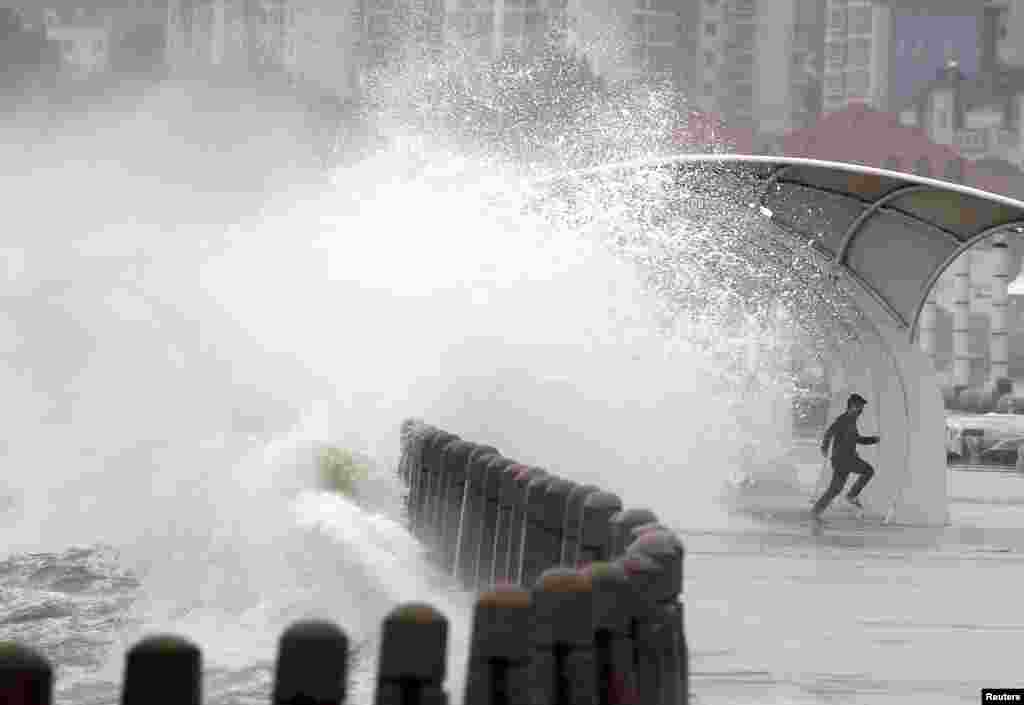 Seorang pria berlari sementara gelombang yang ditiup angin melewati penghalang di pantai Yantai, Provinsi Shandong, China.