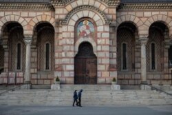 FILE - People walk past St. Marko's church during a curfew imposed to prevent the spread of coronavirus disease (COVID-19) in Belgrade, Serbia, April 21, 2020.