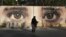 FILE - An Afghan woman waits for transportation in front of street art on a barrier wall of the NDS (National Directorate of Security) in Kabul, Afghanistan, Aug. 20, 2015. A group called the Art Lords created the eyes on the NDS wall as a warning to corrupt officials.