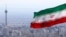 FILE - Iran's national flag flutters in the wind as the Milad telecommunications tower and buildings are seen in the background, Tehran, Iran, March 31, 2020. 