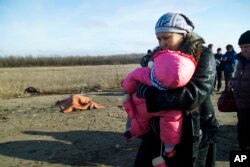 Seorang perempuan dan anaknya serta orang-orang lain lagi melewati mayat seorang pria yang tewas akibat ranjau darat dekat tempat penyeberangan ke daerah yang dikuasai pemerintah Ukraina, dekat Donetsk, Ukraina (10/2).