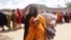 A woman, who fled amid a drought, carries her baby at a makeshift camp for displaced people on the outskirts of Mogadishu, Somalia on Tuesday, Sept. 26, 2023.