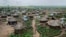 FILE - Women and children return home with plastic containers of water, in a section of the sprawling complex of mud-brick houses and tents that makes up the Bidi Bidi refugee settlement in northern Uganda, June 9, 2017.